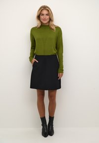 Green knit sweater with ribbed cuffs and a V-pattern design, paired with a black A-line skirt featuring pockets and a smooth texture. Black ankle boots.
