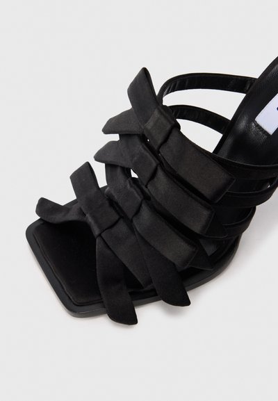 Sandale noire à talon haut avec un bout carré et plusieurs brides en satin superposées en forme de nœud à l'avant et à la cheville.