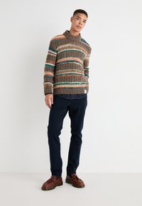 Suéter de punto con rayas horizontales multicolores en marrón, verde azulado, naranja y amarillo; cuello de caja de punto acanalado y puños; combinado con pantalones oscuros y zapatos.