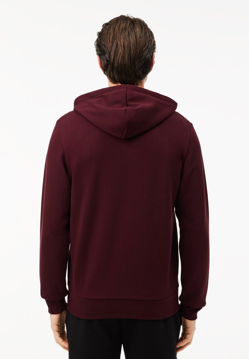 Haut à capuche bordeaux avec cordon de serrage, manches longues et poignets côtelés. Fabriqué en tissu doux et lisse avec une coupe décontractée.