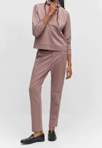 Sudadera rosa con cuello alto, combinada con pantalones a medida a juego, ambos hechos de tela suave. Calzado incluye mocasines negros.