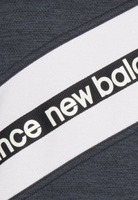 Tessuto atletico grigio con una striscia bianca, decorato con un nastro nero su cui è scritto "new balance" in bianco. Superficie testurizzata.