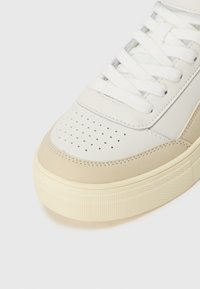 Witte leren sneaker met een beige rubberen zool. Kenmerken zijn onder andere een geperforeerde teenbox en textuuraccenten op de zijkanten en de hiel.