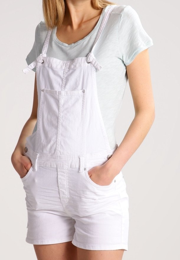 Vita denimoveraller med justerbara axelremmar, framfickor och uppvikta shorts, i kombination med en ljusblå kortärmad skjorta.