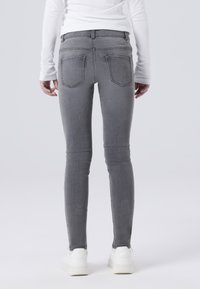 Sive uske traperice s klasičnim dizajnom od pet džepova, srednjim pojasom i suptilnim šavovima. Nosive s bijelim tenisicama, glatka denim tekstura.