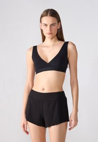 Bralette sportivo nero con scollo a V profondo e spalline larghe, abbinato a pantaloni corti neri a coste con orlo a scallop e cintura elastica.