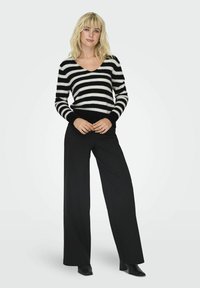 Gestreifter V-Ausschnitt-Pullover in Schwarz und Weiß mit langen Ärmeln, kombiniert mit schwarzen weiten Hosen und schwarzen Absatzstiefeln. Weicher Stoff, lässiger Schnitt.
