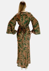 Lang, grøn satin kjole med blomsterdesign i brune nuancer, der har brede trompetærmer og et bælte i taljen for en tætsiddende silhuet.