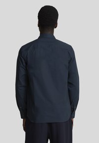 Camicia da uomo blu navy scuro con bottoni, maniche lunghe, colletto e una trama liscia, caratterizzata da un design con schiena dritta e polsini con bottoni.