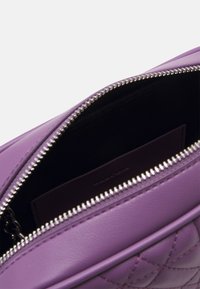 Borsa in pelle viola con una texture liscia e un motivo trapuntato. Presenta una zip argentata e una fodera interna scura.