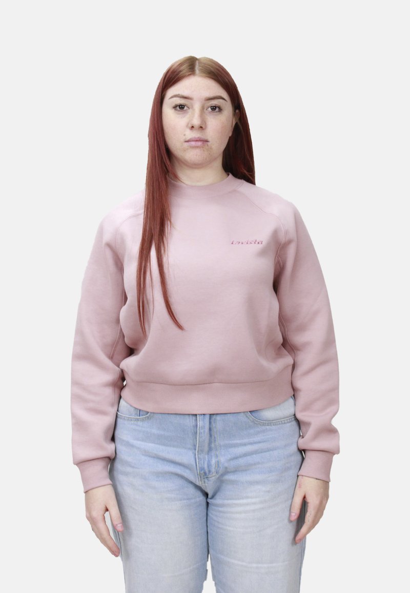 Felpa rosa con scollo rotondo e maniche lunghe, realizzata in tessuto morbido. Presenta un orlo a coste e un dettaglio logo sottile. Indossata con jeans azzurri.