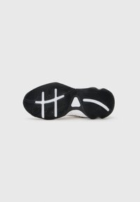 Semelle de sneaker en caoutchouc noir avec une surface texturée, dotée d'accents blancs et d'un design distinctif, comprenant des motifs croisés et un détail triangulaire.