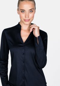 Marineblaue Knopfleiste mit Stehkragen, langen Ärmeln und glatter Textur. Mit fünf schwarzen Knöpfen auf der Vorderseite.