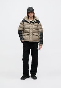 Kurtka puchowa w beżowym i czarnym kolorze, z zamkiem błyskawicznym z przodu, dwoma kieszeniami oraz wysokim kołnierzem. Połączona z czarnymi spodniami cargo i czarnymi butami.