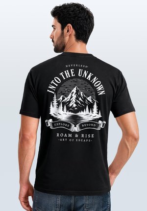Mann mit dunklen Haaren trägt ein schwarzes T-Shirt mit einem weißen Berg, Bäumen, Vögeln und dem Text "Into the Unknown, Explore Beyond, Roam & Rise."