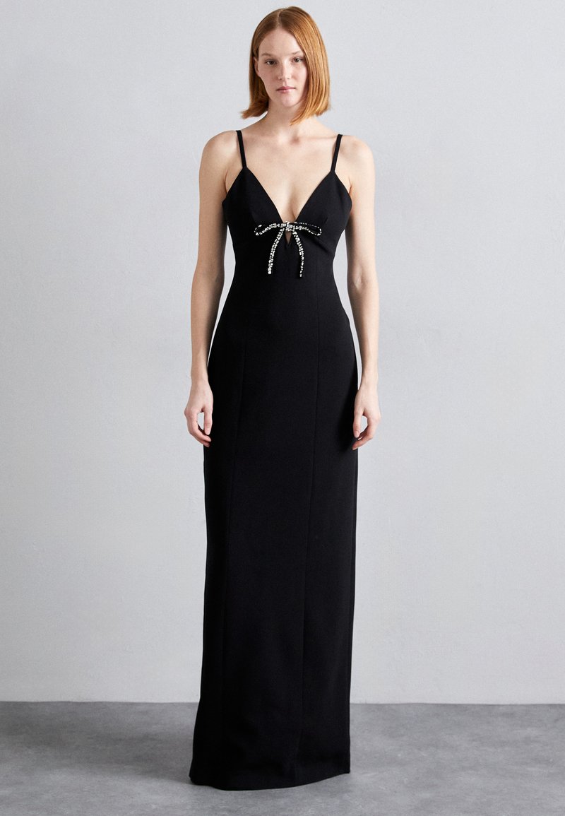 Black, fitted maxi dress with thin straps and a deep V-neck. Features a decorative bow made of rhinestones at the chest. Smooth texture.