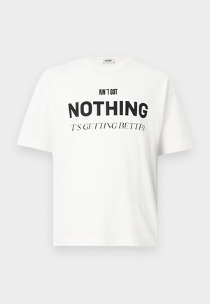 Camiseta blanca de gran tamaño con el texto negro "NO TENGO NADA, ESTÁ MEJORANDO" impreso en la parte frontal, mangas cortas, escote redondo.