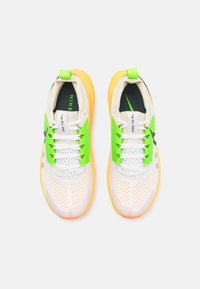 Chaussures de sport blanches avec des accents verts et des semelles orange néon. Elles présentent une tige en mesh, des détails à motifs et des lacets contrastants.