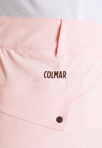 Ljust rosa tygbyxor med en bakficka, sömdekor och en brun "COLMAR"-logotyp. Slät textur och skräddarsydd design.