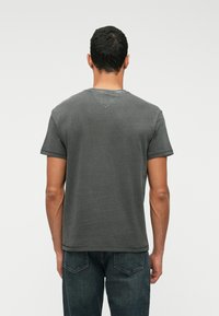 Γκρίζο κοντομάνικο T-shirt με στρογγυλή λαιμόκοψη και V-σχήματος λεπτομέρεια στην πλάτη, φτιαγμένο από βαμβάκι με λεία υφή. Συνδυάζεται με σκούρα τζιν.