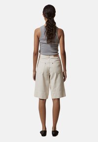 Pantalones cortos hasta la rodilla en color beige claro, fabricados con un tejido texturizado, que cuentan con dos bolsillos traseros y una cinturilla ajustada, combinados con una camiseta sin mangas gris.
