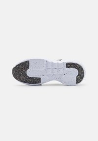 Semelle de chaussure blanche avec des patchs d'adhérence noirs tachetés au niveau du talon et des orteils, montrant un motif de bande de roulement texturé sur un fond uni.