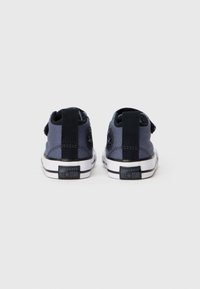 Converse All Star tenisice, tamnoplava platnena tkanina, niska dizajn, crni detalji, čičak trake, bijele gume potplate, logo na peti.