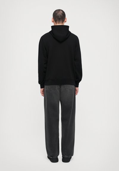 Un sweat à capuche noir et un jean gris foncé à coupe ample. Le sweat a une coupe mi-longue et des poignets côtelés. Le jean ample possède des poches classiques.