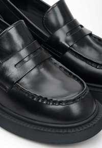 Zwarte leren loafers met een gestikt ontwerp, een gladde textuur en een dikke rubberen zool met een geribbeld patroon. Inclusief elegante riemdetails.