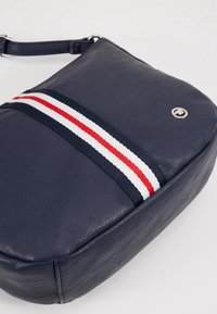 Granatowa skórzana torba na ramię z poziomym wzorem w czerwone i białe paski, srebrnymi akcentami i eleganckim, prostokątnym kształtem.