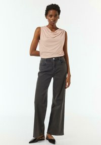 Helles rosa Oberteil mit Cowl-Neck, kombiniert mit hoch taillierten, weiten, dunkelgrauen Jeans. Das Outfit zeichnet sich durch glatte Texturen und minimalen Details aus.