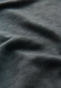 Tejido texturizado en gris oscuro con un sutil patrón geométrico, presentando una superficie suave y una reflexión de luz variada.