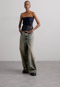 Top blu navy senza spalline con design a strati, abbinato a jeans blu chiaro a gamba larga e scarpe con piattaforma nere. Tessuti lisci e texture visibili.