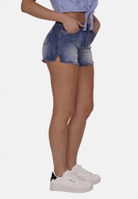Shorts in denim con orlo sfrangiato, colore blu degradé, con tasche frontali e hardware in tono oro. Abbinati a sneakers bianche e una maglietta a righe.