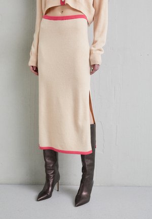 Strikket beige midiskjørt med rosa midje og kantdetaljer, med sidelommer og parret med glinsende brune støvler som går over knærne.