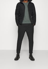 Chaqueta acolchada negra con un diseño estructurado, camiseta de manga larga gris, pantalones negros ajustados y botas negras robustas. Texturas suaves en todo.
