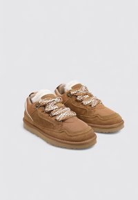 Zapatillas de ante marrón y malla con paneles texturizados, suelas gruesas y cordones estampados con forro interior blanco.