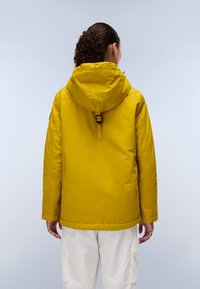 Gelbe wasserdichte Jacke mit Kapuze, ausgestattet mit einem Zugband und seitlichen Taschen, kombiniert mit weißen Cargo-Hosen. Glatte Textur und strapazierfähiges Material.