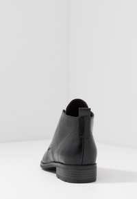 Botte noire en cuir à hauteur de cheville avec une texture lisse, un bout rond et une languette à l'arrière, reposant sur un petit talon empilé.