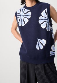 Granatowy bezrękawnik z dzianinowym kwiatowym wzorem w jasnoniebieskim i białym kolorze. Posiada ściągacze przy szyi i u dołu oraz teksturowaną tkaninę.