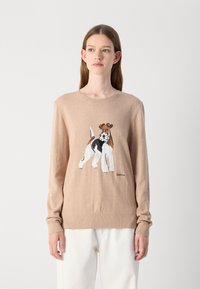 Pulover tricotat bej cu guler rotund. Prezintă un design brodat cu un câine pe față și manșete cu nervuri. Eticheta brandului este vizibilă la tiv.