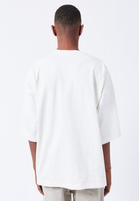 Bílé oversized tričko s krátkými rukávy, vyrobené z bavlny, s jednoduchým designem a pohodlným střihem. Vhodné pro každodenní nošení.