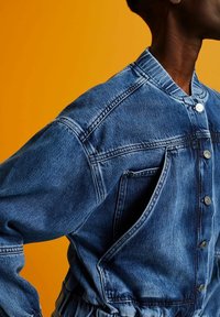 Jeansjacka i medelblått med mandarin-kraag, tryckknappar och elastisk midja med dragsnodd. Har strukturerade axlar och sidofickor.