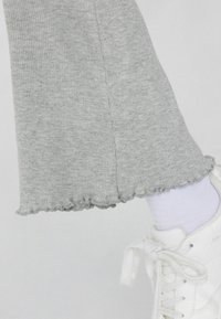 Graue gerippte Hose mit gewelltem Saum, kombiniert mit einem weißen Sneaker und einem helllila Socken. Fokussiert auf die Textur und die einzigartigen Säumedetails.