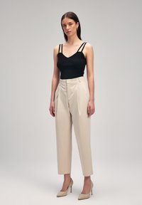 Top a maniche sottili nero a costine, abbinato a pantaloni beige a vita alta e scarpe con tacco nudo. Linee semplici e pulite.