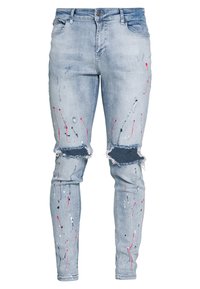 Jeans de mezclilla deslustrados de color azul claro con rodilleras rasgadas, presentando patrones de salpicaduras de pintura en rosa, azul marino y blanco para un diseño único.