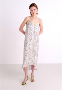 Slip dress dengan pola bunga, tali spaghetti, dasar krem, dengan desain biru dan beige. Memiliki hem tinggi-rendah. Dipadukan dengan sepatu hak tinggi strap hijau.