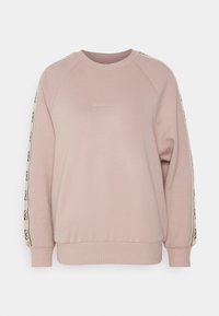 Sweat-shirt rose clair avec des manches raglan, portant un petit logo "GUESS" à l'avant et un ruban à motif le long des coutures latérales.