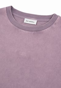 T-shirt lavande à col rond avec col côtelé, arborant un logo brodé « OH APRIL » en fil assorti sur la poitrine et une étiquette imprimée à l'intérieur.