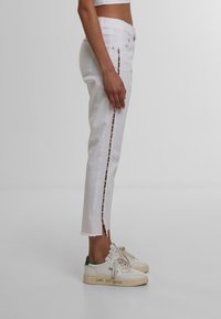 Valged denim püksid sirge lõikega, külje lukuga ja leopardimustriga aksessuaari. Rebenenud allserv; koos valgete ja roheliste tossudega.